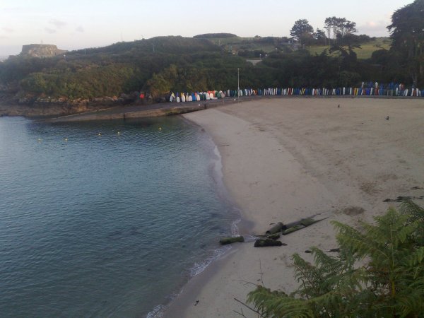 A view from a cliff across a small sandy beach with a falling tide